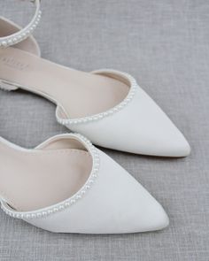 a pair of white shoes with pearls on the toe and heel are sitting on a gray surface