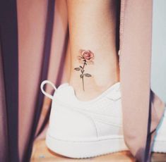 a woman's foot with a small rose tattoo on her left ankle and behind her is a white tennis shoe