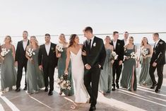 a group of people standing next to each other in front of the ocean with bouquets