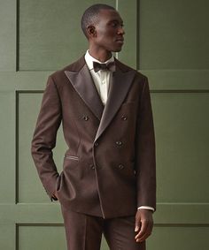 a man in a brown suit and bow tie standing next to a green garage door