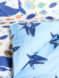 a bed with blue and white sheets that have fish printed on them, along with two pillow cases