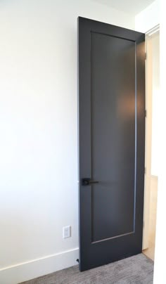 an empty room with a black door and carpeted floor in front of the wall