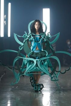 a woman is walking down the runway in a dress made out of blue and green paper