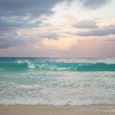 an ocean view with waves crashing on the shore and clouds in the sky above it