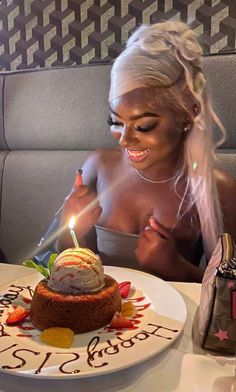 a woman sitting at a table in front of a cake with a lit candle on it