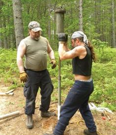 two men in the woods are working on a metal pole with one man holding a drill