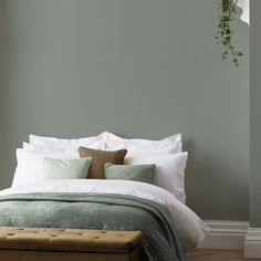 a bed with white and green pillows in a bedroom next to a plant hanging on the wall