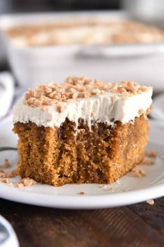 a piece of carrot cake with white frosting and chopped nuts on top, sitting on a plate