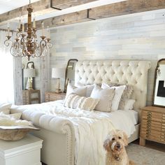 a white bed sitting under a chandelier next to a wooden floor covered in pillows