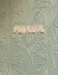 the word prada is lit up in front of a white wall with flowers and leaves