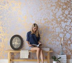 a woman sitting on top of a wooden bench next to a wall covered in gold paint