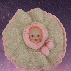 a baby doll in a crocheted hat and mittens on top of a blanket