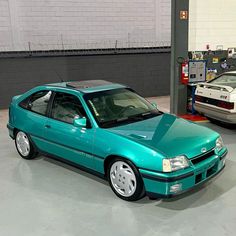 a blue car parked in a garage next to another car on the ground with other cars behind it