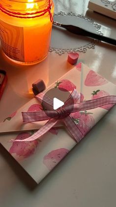 a candle and some candy are sitting on a table next to an envelope with a pink ribbon