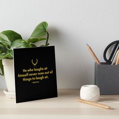 a black and yellow quote on the side of a white wall art boarder next to a potted plant