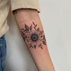 a woman's arm with a sunflower and leaves tattoo on the left forearm