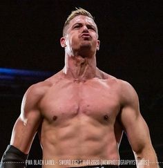 a man without a shirt standing in the middle of a wrestling ring with his hands on his hips