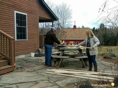 two people standing around a picnic table in front of a house