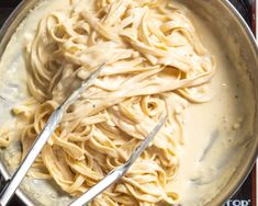 a pan filled with pasta and sauce on top of a stove burner next to two tongs