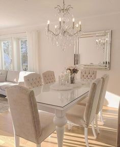 a white dining room table with chairs and a chandelier hanging from the ceiling