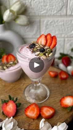 two glasses filled with yogurt and strawberries on top of a wooden table