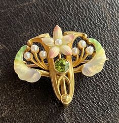 An enchanting Art Nouveau era flower pin by American maker Whiteside & Blank with iridescent enameling and a peridot center.  The soft pink petals remind us of cherry blossoms while the green enameled leaves look like samara seeds!  Wonderfully detailed with pearl accents.  The pin is stamped with the maker’s mark along with faded marks for 14K stamps. Metal: 14K Yellow Gold Weight: 6.1 grams Measurement: 1 inch long by 1.1 inches wide Markings: Maker’s mark Condition: In very good antique condition with some minor surface wear consistent with age.  One petal may have had the enamel touched up previously. Follow us on Instagram @alphaomegajewelry for the latest updates from our shop!  We have lots of fun there and add videos, highlights, and showcase our newest acquisitions. Art Nouveau Jewelry Vintage, Nouveau Jewelry, Vintage Jewelry Art, Egyptian Revival, Pin Art, Art Nouveau Jewelry, Diamond Brooch, Bird Jewelry, Crown Jewels