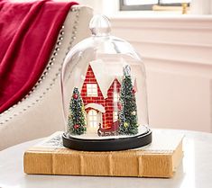 a snow globe with a house under it on top of a table next to a chair