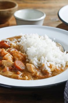 a white plate topped with rice and meat covered in gravy on top of a wooden table