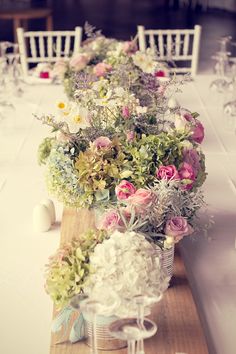 the table is set with white and pink flowers in vases on wooden planks