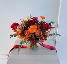 a vase filled with lots of flowers on top of a white table next to a red ribbon