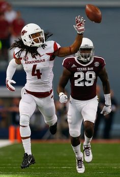 two football players are jumping in the air with their hands up and one is holding a ball