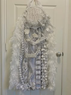 a door hanger decorated with white feathers and an elaborate number on it's front