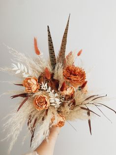 a hand holding a fake flower arrangement with feathers and flowers on it's head