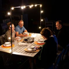 a group of people sitting around a wooden table with plates and bowls on top of it