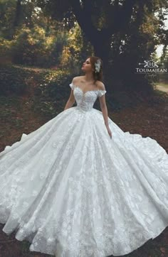 a woman in a white wedding dress standing on the grass with her hands behind her back