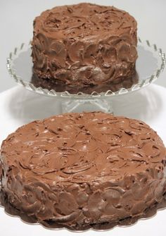 two chocolate cakes sitting on top of a white cake platter next to each other