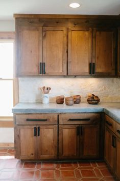 a kitchen with wooden cabinets and tile flooring in front of a window, along with two bowls on the counter