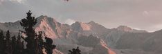 an airplane is flying over the mountains on a cloudy day with trees in foreground