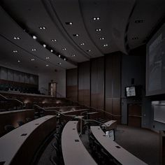 an empty lecture hall with rows of desks and projector screens on the wall