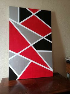 a painting on a wooden table with a white wall in the background and a black, gray, red and grey abstract design