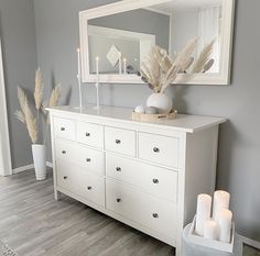 a white dresser with candles on top and a mirror above it in a gray room