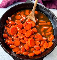 a skillet filled with cooked carrots and gravy next to a wooden spoon