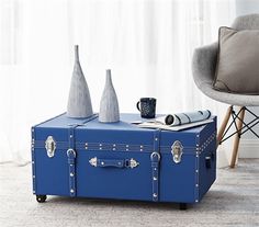 a blue suitcase sitting on top of a wooden table next to a chair and vases