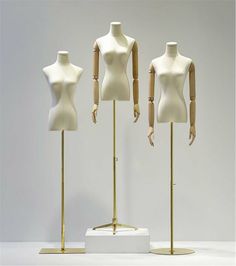 three mannequins are standing next to each other on wooden bases in front of a white wall