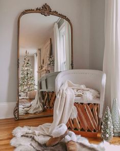 a mirror sitting on top of a wooden floor next to a white chair and christmas tree