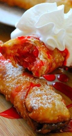 two pastries covered in whipped cream and toppings on a wooden cutting board with red sauce