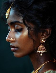 a woman wearing gold jewelry and looking off to the side with her eyes closed, in profile