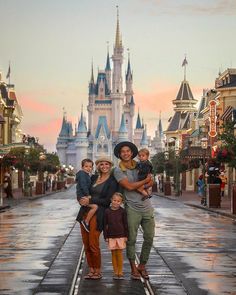 a man and woman with two children standing in front of a castle at disney world