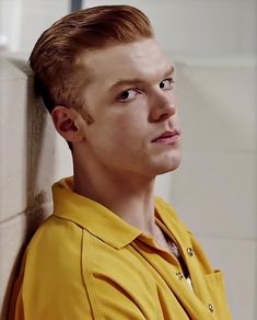 a young man in a yellow shirt leaning against a wall with his head turned to the side