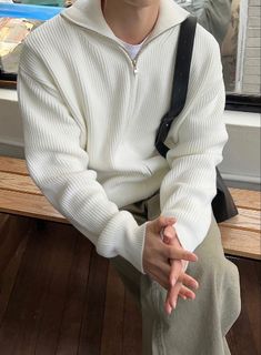 a young man sitting on a bench wearing a white sweater and khaki pants